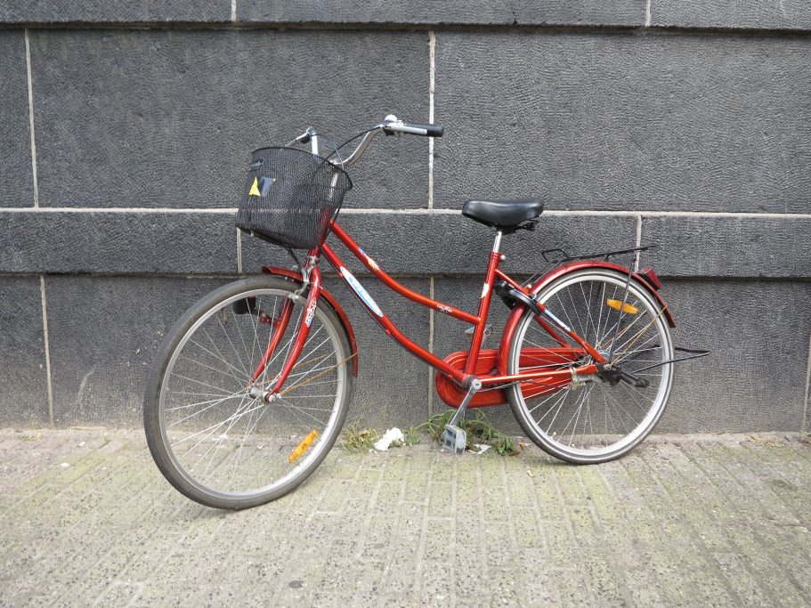 Bizikleta bat Amsterdamgo kale batean, horma ilun baten kontra jarrita, argazkia egin eta saltzeko iragarkian txertatzeko.