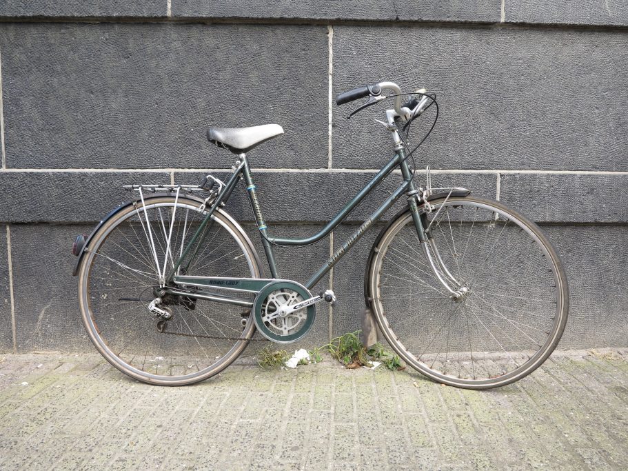 Bizikleta bat Amsterdamgo kale batean, horma ilun baten kontra jarrita, argazkia egin eta saltzeko iragarkian txertatzeko.