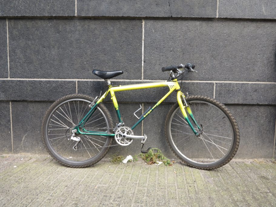 Bizikleta bat Amsterdamgo kale batean, horma ilun baten kontra jarrita, argazkia egin eta saltzeko iragarkian txertatzeko.