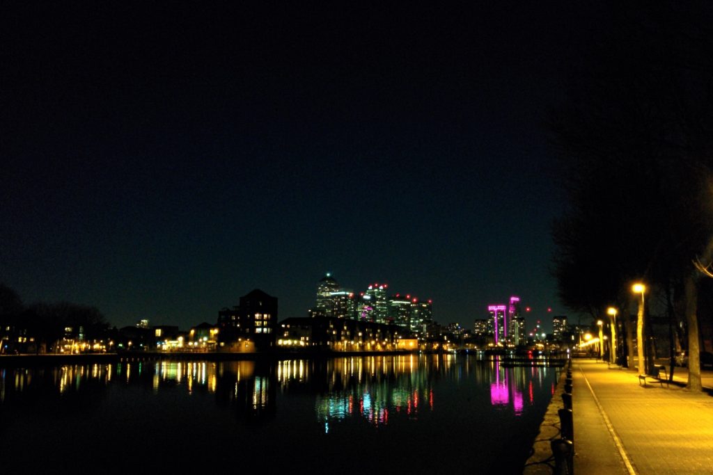 Canary Wharfeko etxeorratzen gaueko ikuspegia Surrey Quaysetik ikusita, argiak Greenland Docken islatzen direla.