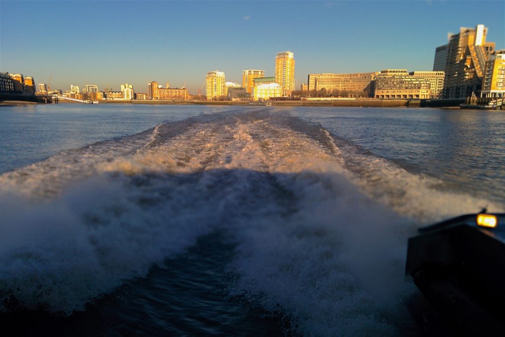 Ontziak sortzen dituen olatuak Thames ibaian, Canary Wharf atzean utzita, neguko goiz eguzkitsu batean.