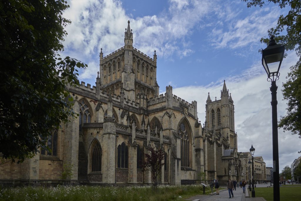 Arkitektura gotikoan eraikitako katedral baten argazkia, kaletik eginda. Inguruko lorategian jendea dabil. Zeruan hodeiak eta urdinguneak daude.